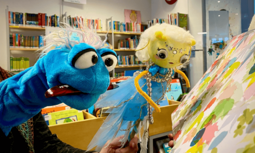 Zwei Plüschhandpuppen mit Bücherregalen im Hintergrund