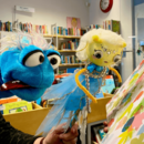 Zwei Plüschhandpuppen mit Bücherregalen im Hintergrund