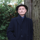 Mann mit Hut steht vor Bäumen