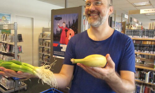 Mann hält Lauchzwiebeln und eine Banane in der Hand