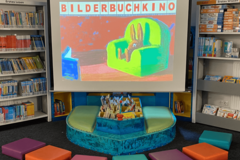 Eine Leinwand mit dem Slogan "Bilderbuchkino", davor bunte Sitzkissen
