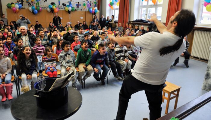 Mann macht Späße vor einer Schulklasse und die Kinder lachen
