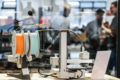 Im Vordergrund ist ein Gerät des Makerlab, im Hintergrund sind verschwommen einige Menschen zu sehen
