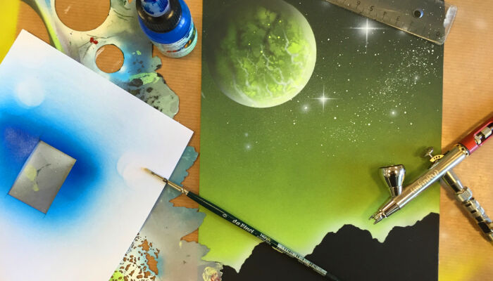 buntes Foto zeigt Farbtopf, Pinsel, Airbrush-Pinsel und Lineal drapiert um Kunstwerk, das offensichtlich mit Airbrush hergestellt wurde