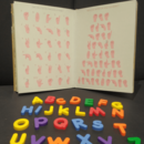 Ein Buch, dass das Fingeralphabet abbildet. Davor liegen bunte Buchstaben.