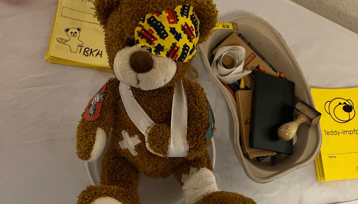 Ein Teddybär liegt bandagiert und mit Pflastern an Kopf und Bauch auf einem Behandlungstisch.