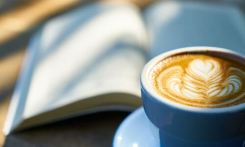 Ein aufgeschlagenes Buch, davor eine Tasse Cappucino