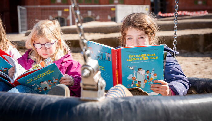 zwei Mädchen mit Buch in Schaukel