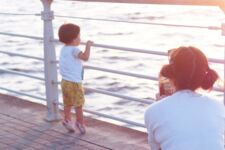 junger Mensch schaut aufs Meer und wird von älterem Menschen mit einem Smartphone fotografiert