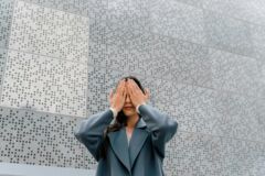 Eine Frau hält sich die Augen zu vor einer Wand mit Brailleschrift