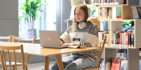 Eine Frau sitzt vor einem Bücherregal an einem Laptop