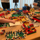 Kinder stehen um einen Tisch herum, auf dem ein Flughafen aus LEGO aufgebaut wurde. Im Hintergrund ist ein IPad ist auf einem Stativ als Kamera auf den Tisch gerichtet.