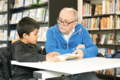 Mann hilft Kind beim Lesen lernen in der Bücherhalle