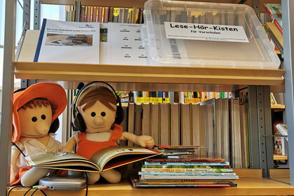 Zwei Puppen mit Kopfhörern und Bilderbuch