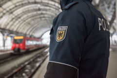 Foto-Bildausschnitt zeigt die Jacke eines Polizisten, der am Bahnhof gegenüber eines Zuges steht