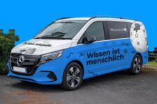 Blaues Wikipedia-Auto vor blauem Hintergrund. Der Schriftzug auf dem Auto lautet: Wissen ist menschlich".