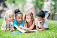 4 lesende Kinder im Gras