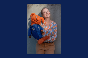 Frau mit oranger Handpuppe im Weltall-Anzug