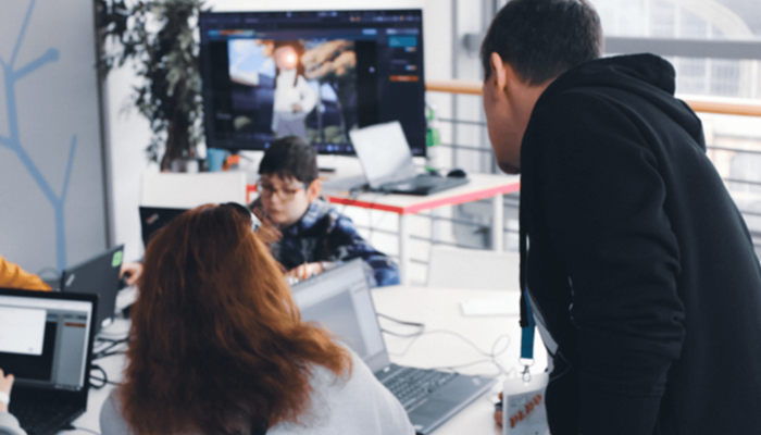 Eine Person blickt einer anderen an einem Scheibtisch mit Laptops über die Schulter