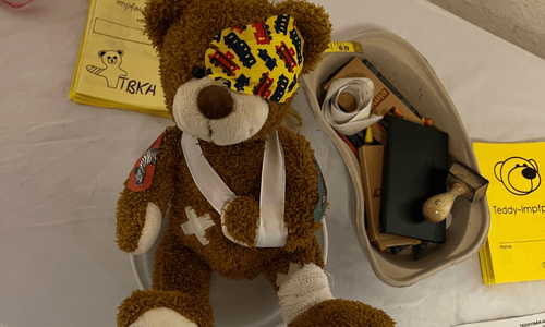 Ein Teddybär liegt bandagiert und mit Pflastern an Kopf und Bauch auf einem Behandlungstisch.