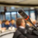 Foto eines Mikrofons mit Publikum im Hintergrund