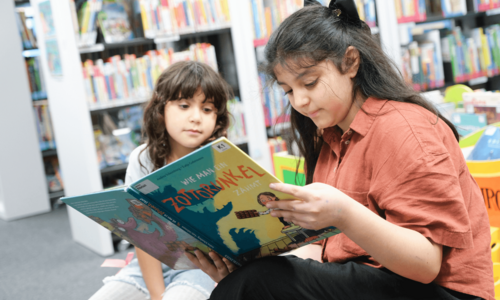Zwei Kinder sitzen in Bücherhalle und lesen in Buch