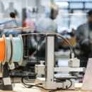 Im Vordergrund ist ein Gerät des Makerlab, im Hintergrund sind verschwommen einige Menschen zu sehen