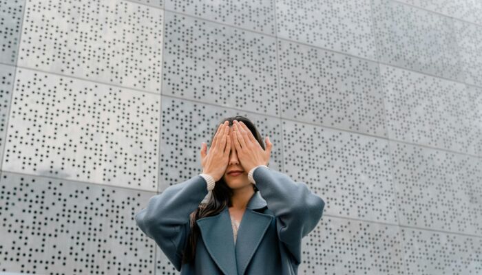 Eine Frau hält sich die Augen zu vor einer Wand mit Brailleschrift