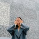 Eine Frau hält sich die Augen zu vor einer Wand mit Brailleschrift