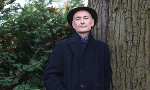 Mann mit Hut steht vor Bäumen