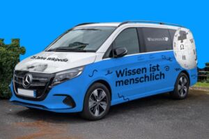 Blaues Wikipedia-Auto vor blauem Hintergrund. Der Schriftzug auf dem Auto lautet: Wissen ist menschlich".