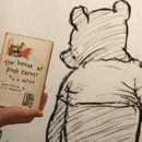 Gezeichneter Winnie Pu und eine Hand, die ein altes Winnie Pu Buch hält