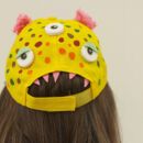 Bild zeigt Hinterkopf eines Kindes mit einer gelben Mütze, die zu einem Monsterkopf umdekoriert wurde