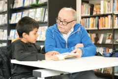 Mann hilft Kind beim Lesen lernen in der Bücherhalle