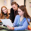 Zwei junge Frauen vor einem Computer bekommen ein Erklärung vom Lehrer