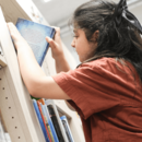 Mädchen stellt Buch in Regal ein