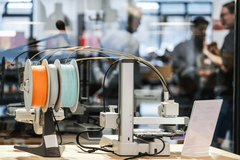 Im Vordergrund ist ein Gerät des Makerlab, im Hintergrund sind verschwommen einige Menschen zu sehen