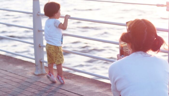 junger Mensch schaut aufs Meer und wird von älterem Menschen mit einem Smartphone fotografiert