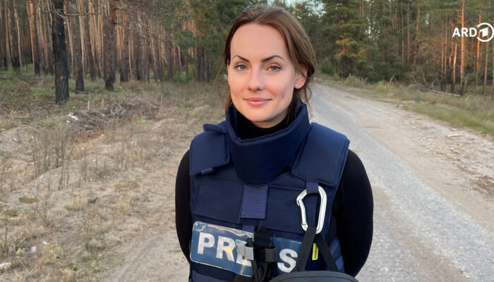 lächelnde jüngere Dame steht in Sicherheitskleidung der Presse auf einem Waldweg