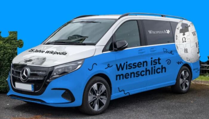 Blaues Wikipedia-Auto vor blauem Hintergrund. Der Schriftzug auf dem Auto lautet: Wissen ist menschlich".