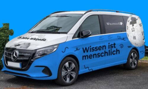 Blaues Wikipedia-Auto vor blauem Hintergrund. Der Schriftzug auf dem Auto lautet: Wissen ist menschlich".