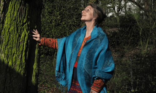 Elita Carstens in der Natur, Hand an einem Baum, nach oben schauend