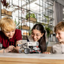 Zwei Kinder und Lehrkraft beobachten einen Roboter
