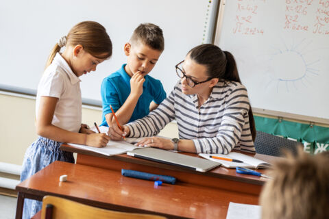 Eine Lehrerin unterrichtet zwei Schulkinder an ihrem Pult