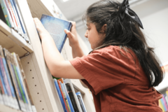 Mädchen stellt Buch in Regal ein