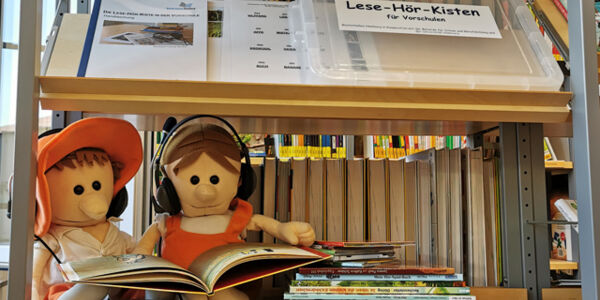 Zwei Puppen mit Kopfhörern und Bilderbuch