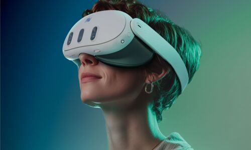 Das Bild zeigt vornehmlich das Gesicht einer Frau, die eine VR-Brille trägt und dabei ihren Kopf leicht nach oben hebt. Sie lächelt. Der Hintergrund zeigt einen Farbverlauf von links (dunkelblau) nach rechts (helles grün).