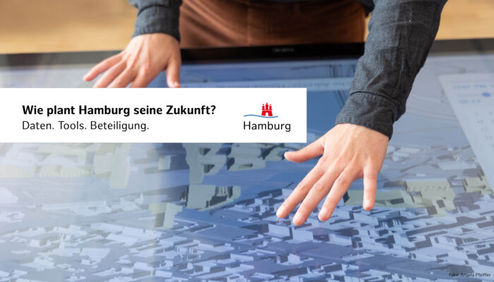 Weibliche Hände mit ausgestreckten Fingern über einem Screen, auf dem ein digitales Stadtplanungsmodell zu sehen ist.
