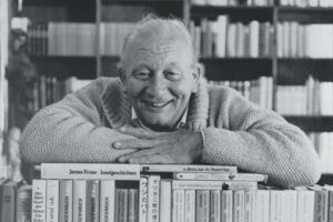 Schwarz-Weiß-Bild von James Krüss auf einem Stapel Bücher.