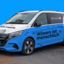 Blaues Wikipedia-Auto vor blauem Hintergrund. Der Schriftzug auf dem Auto lautet: Wissen ist menschlich".